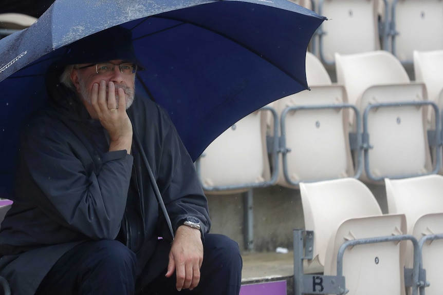 A man sits under an umbrella cupping his chin in one hand