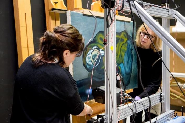 Two people put Pablo Picasso's painting The Crouching Tiger through an x-ray device.