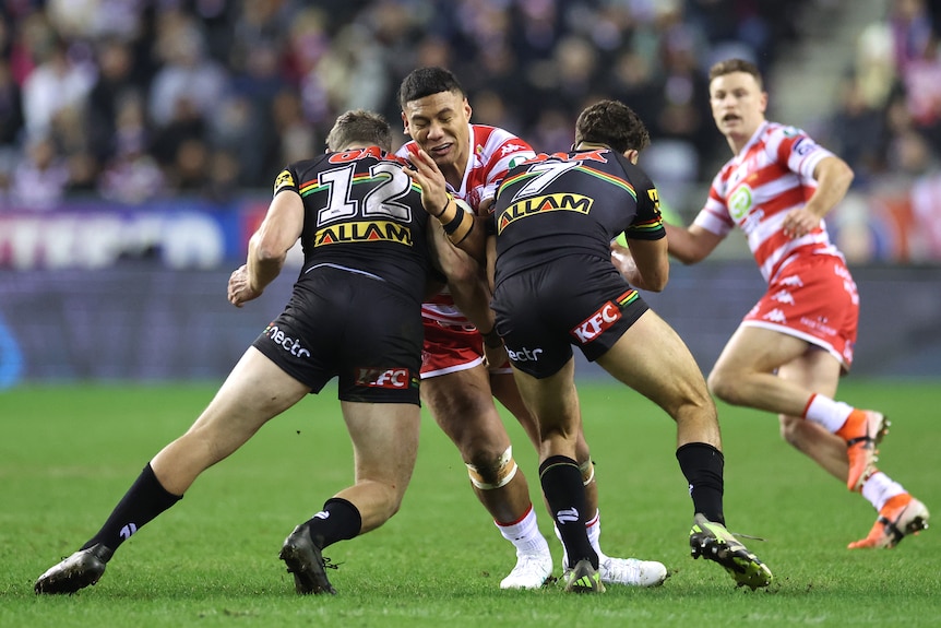 A Wigan player carries the ball as he is tackled by two Penrith players in the World Club Challenge.