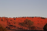 people in the distance on top of a red sand dune
