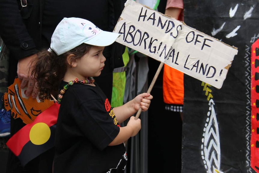 young girl holding a sign that read hands off aboriginal land