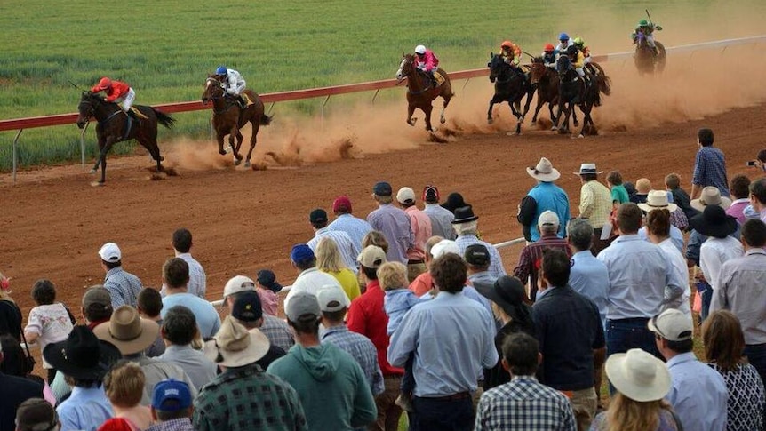 crowd watching horses run on dirt track