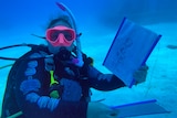 A scuba diver holding up a drawing underwater 