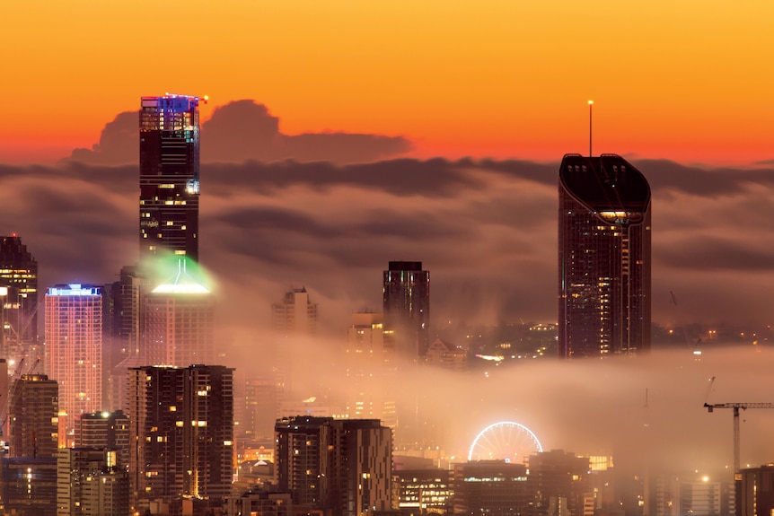 Streaks of Grey fog through high rise buildings against a bright orange morning sky