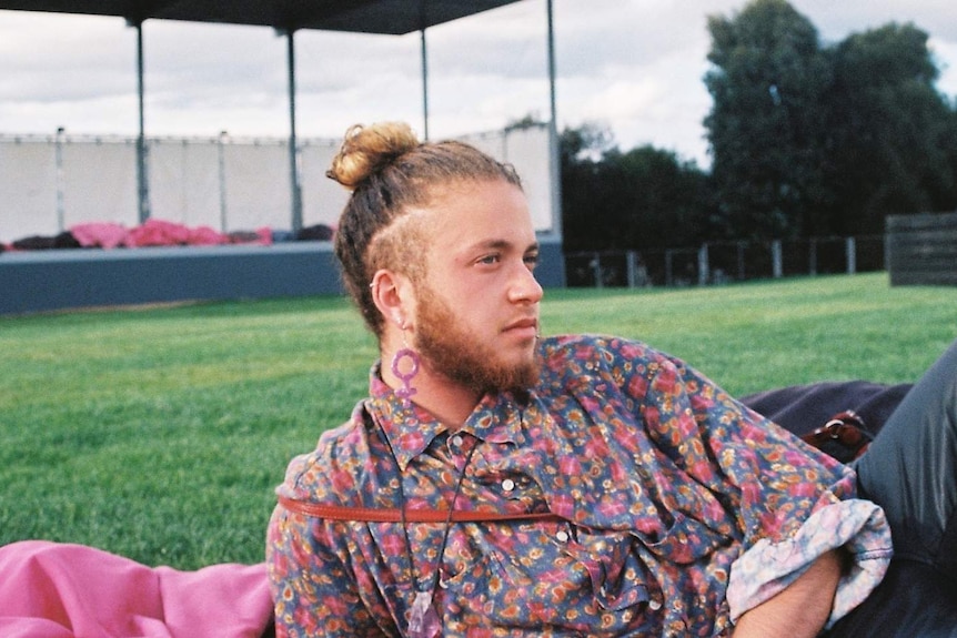 Author and activist Nevo Zisin reclines in a park, wearing a floral shirt. He says he doesn't fear being alone.