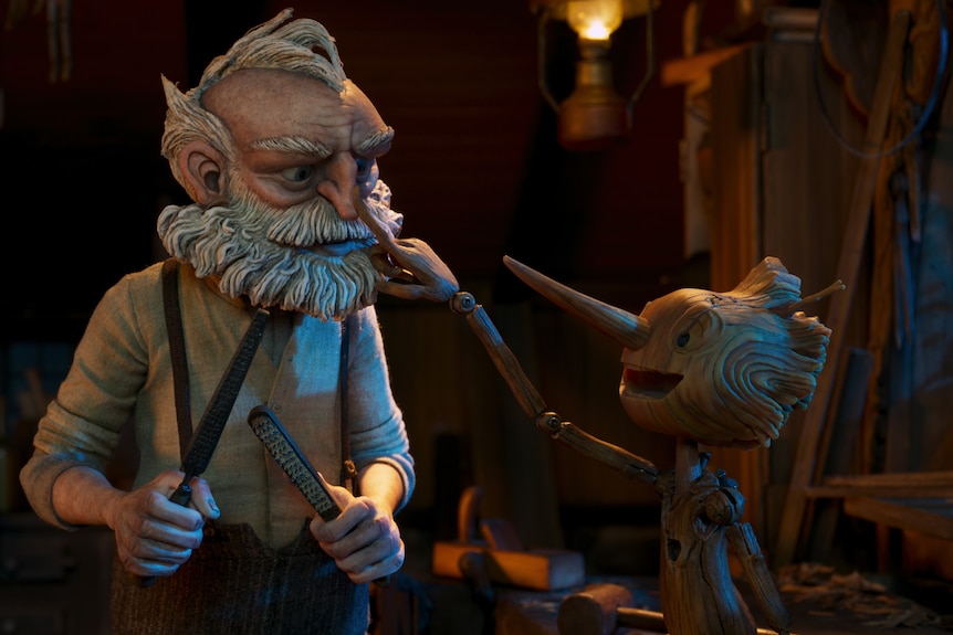 An animated elderly man with white hair and beard is being poked in the face by a small wooden puppet man with a long nose.