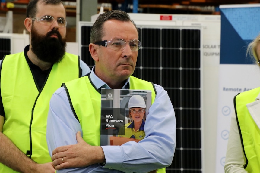 WA Premier Mark McGowan wearing safety glasses and holding a brochure saying 'WA Recovery Plan'.