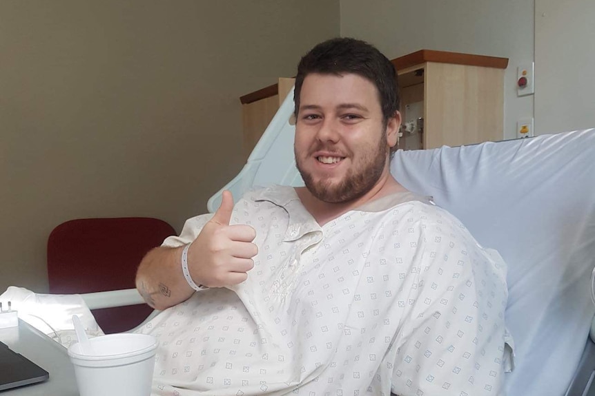 a man in a hospital gown giving a thumbs up from a hospital bed