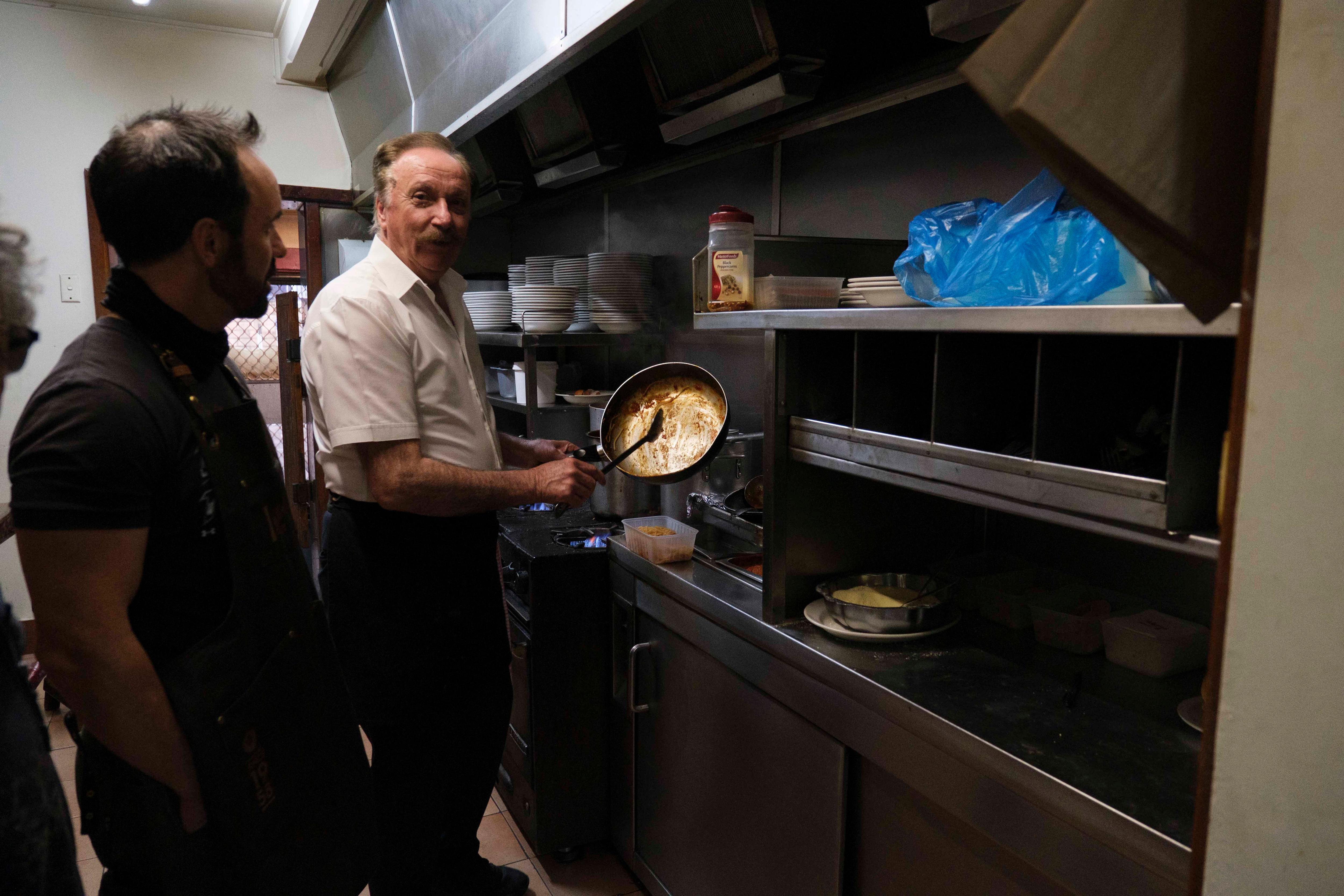 Rocco standing in a kitchen holding up a frying pan.
