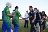 Two rows of girls dressed in cricket tracksuits shake hands as they walk past one another.