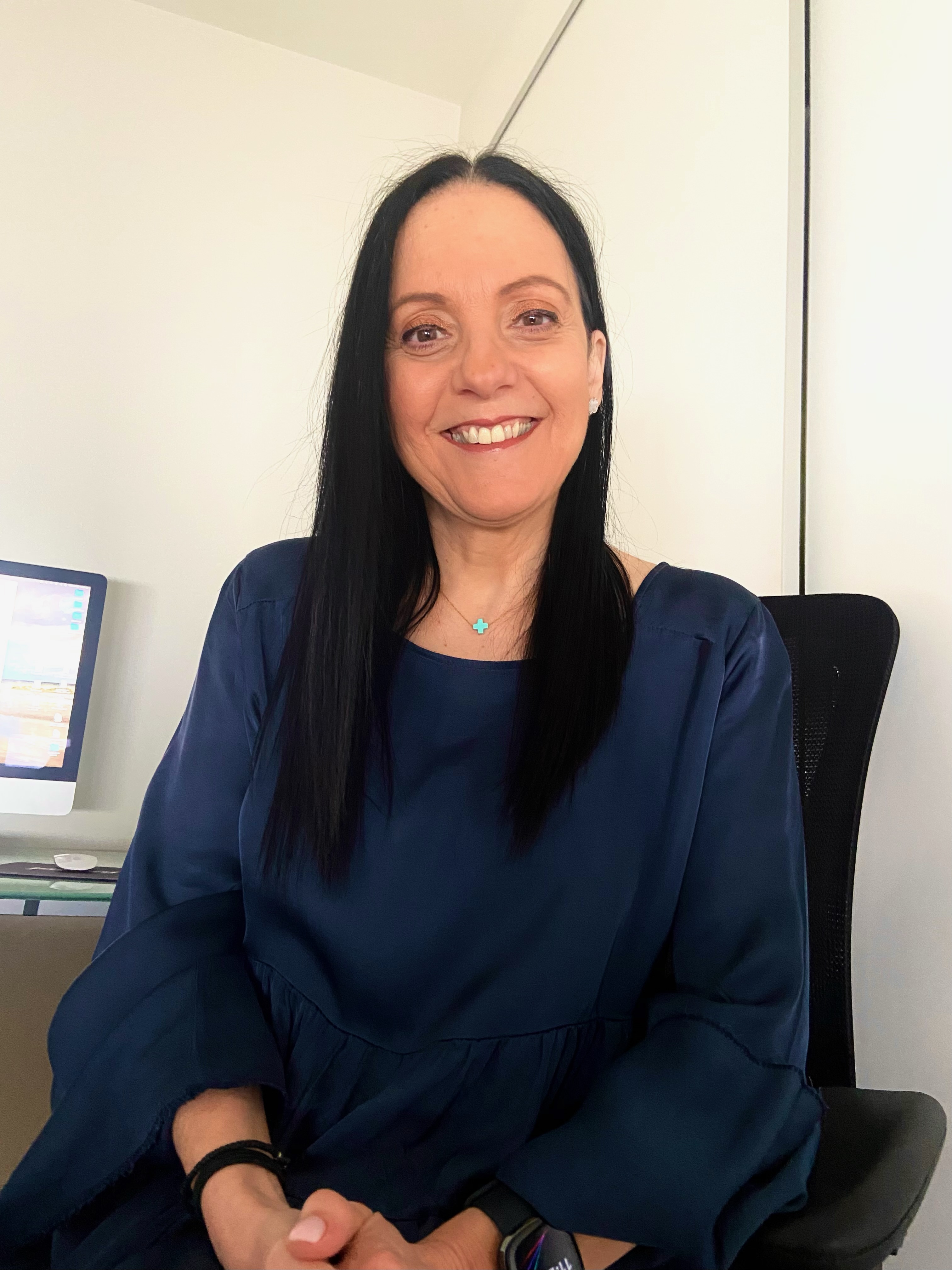 A woman with dark hair sits in a white room