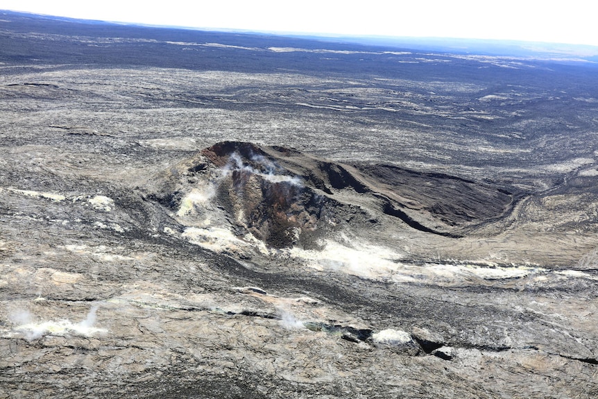 Steam is rising from the ground on top of Mauna Loa’s summit. The ground around is all grey.