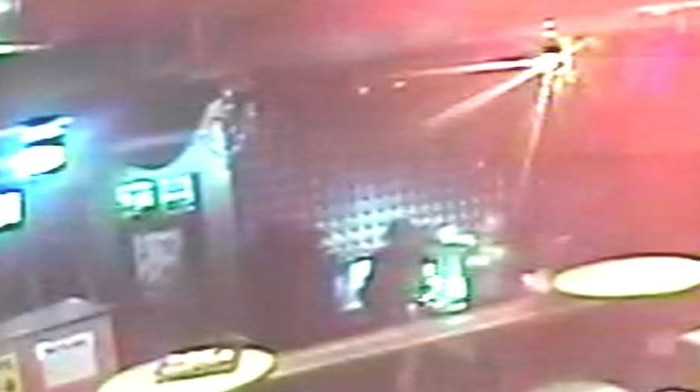 A still from CCTV footage shows red lights across a bar, as white torches are shone on blurry figures at the back.