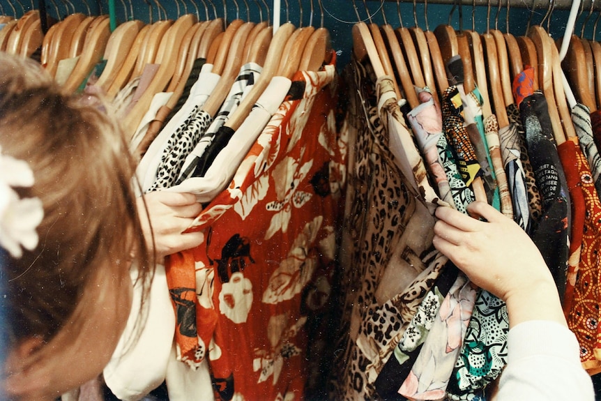 Woman's head is in foreground. She is looking through lots of patterned clothes on hangers.