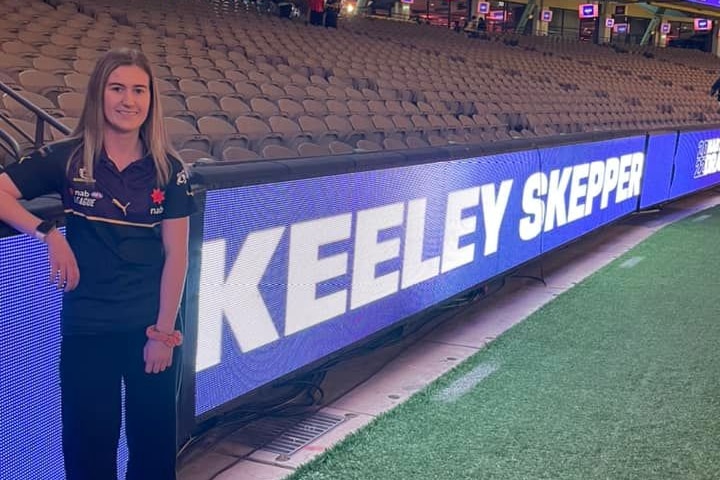 girl stands next to her name on digital banner at footy ground
