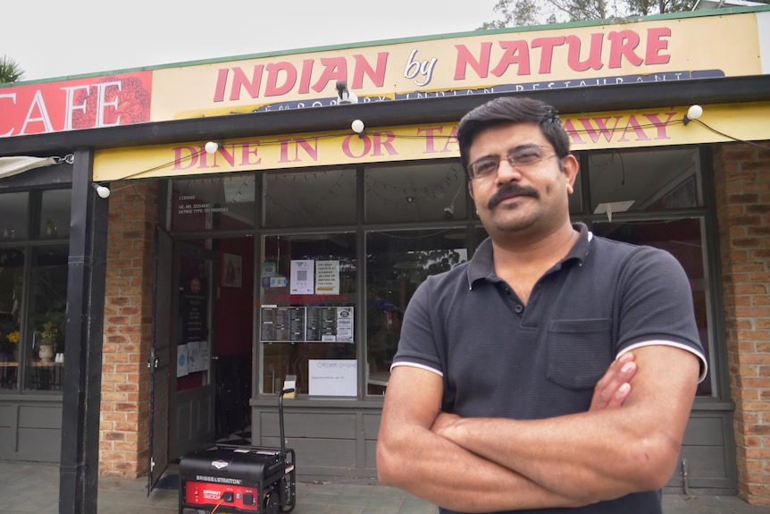 A man standing outside a restaurant with his arms folded.