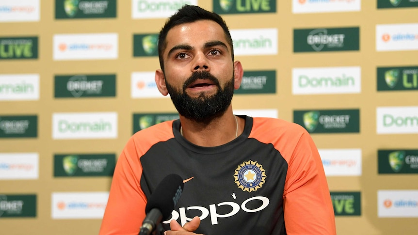 A cricket captain looks out at a crowd of reporters (off camera) waiting for a question.