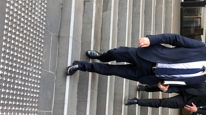 Two men, wearing suits, walk down stairs outside a court house