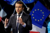 Emmanuel Macron speaks to a crowd with the flag behind him