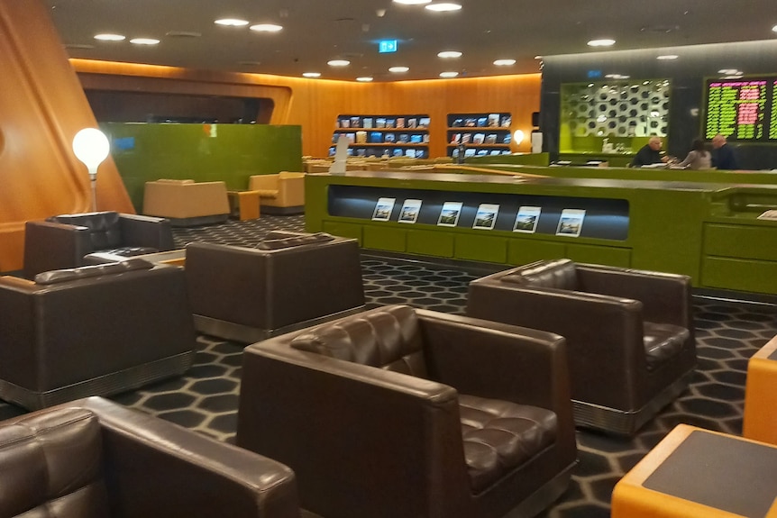 A vertical image of a an airport lounge, with brown leather seats, green counters, and wood accents. 