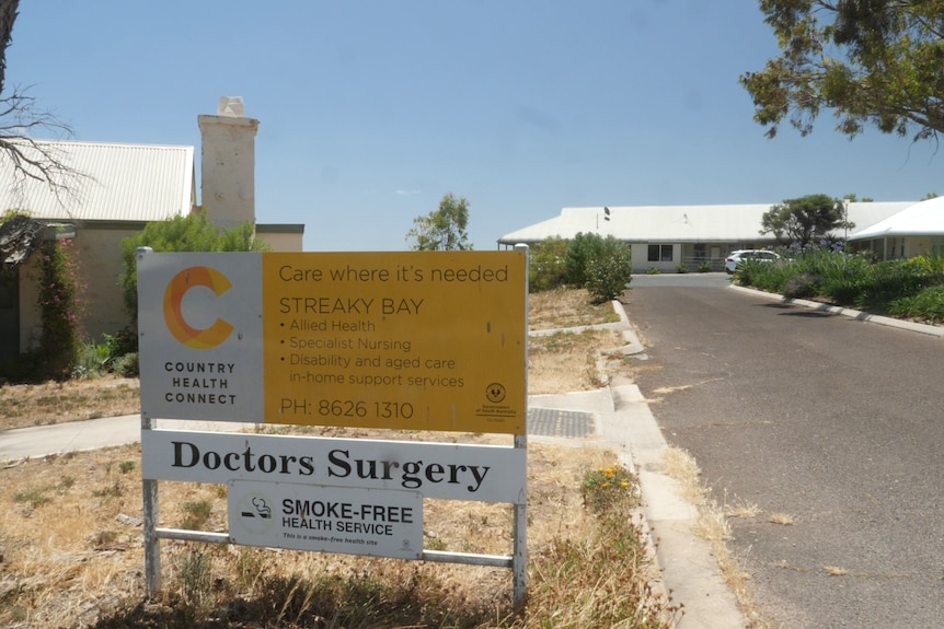 Medical clinic sign, with old cottage ion left and road leading to clinic building on left, trees