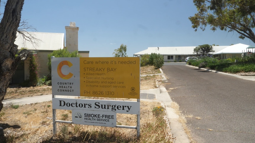 Medical clinic sign, with old cottage ion left and road leading to clinic building on left, trees