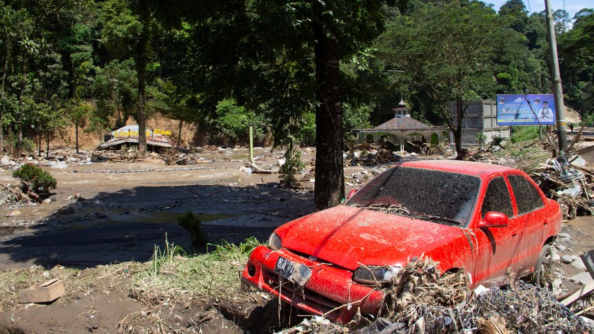 A wrecked red car surrounded by mud and rubbish after floods.