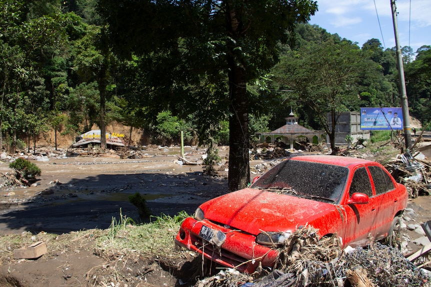 A wrecked red car surrounded by mud and rubbish after floods.