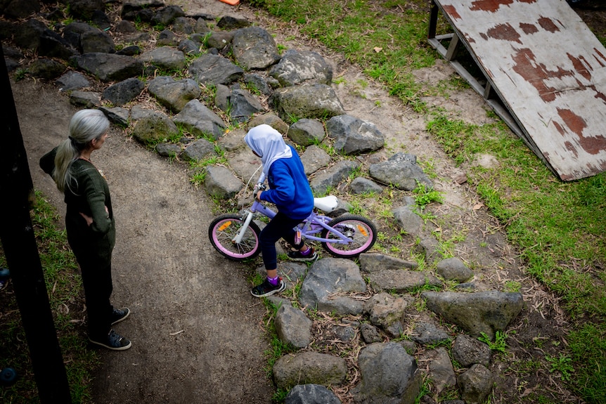 A young girl in a head scarf is seen riding a bike over some large stones