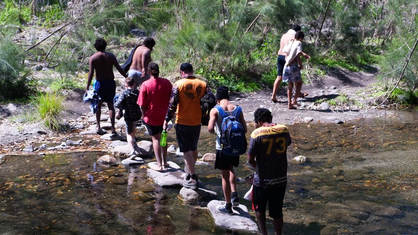 Students walk across stepping stones in a shallow creek