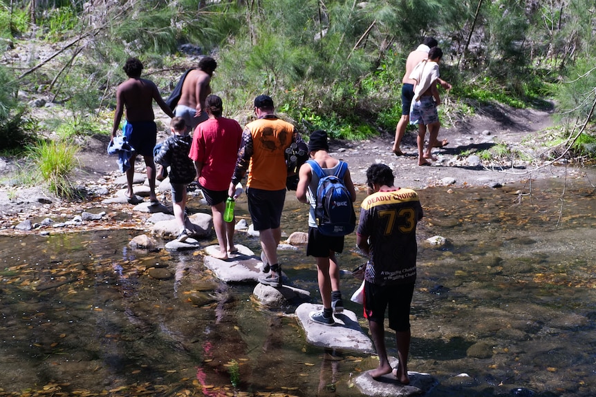 Students walk across stepping stones in a shallow creek