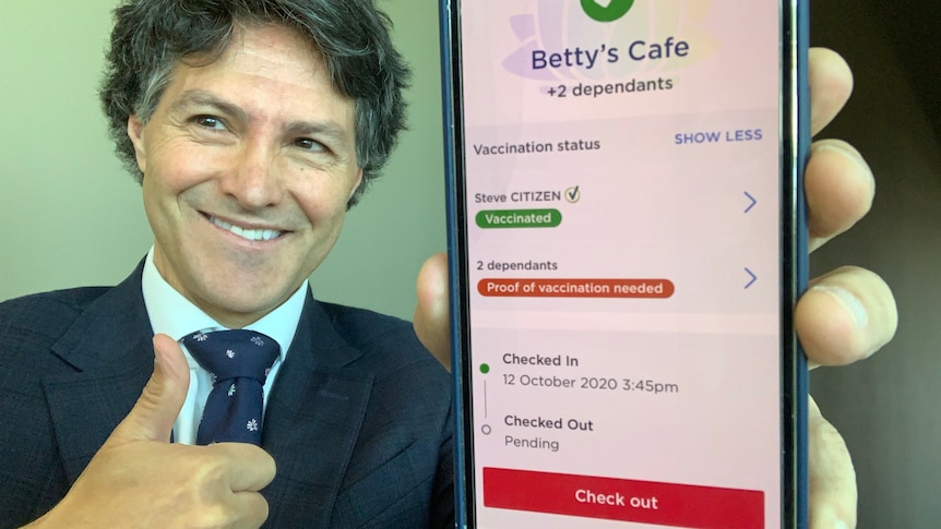 A man in a suit holds a phone showing a person's vaccine status