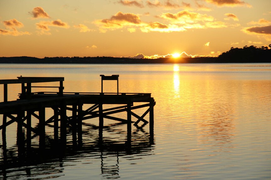Sunrise over a silhouette jetty and calm waters at St Helens in Tasmania.