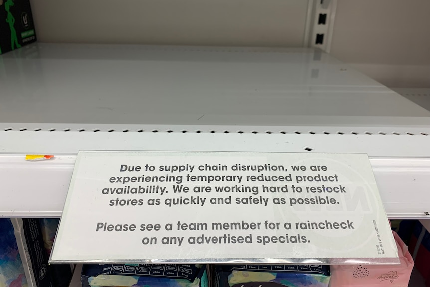 Empty supermarket shelf with a typed sign advertising supply chain issues.
