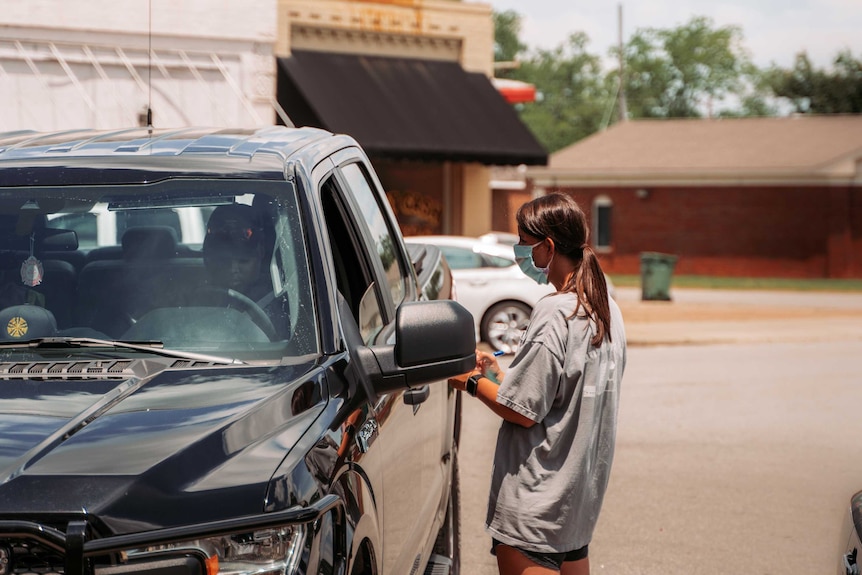 A woman in a face mask talks to a man in a ute