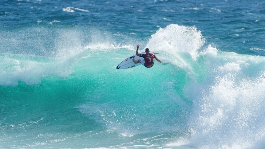 View from a distance of Mick Fanning at the top of a wave which is just about to crest