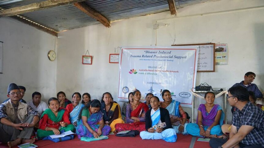 Nepalese people sitting on a mat on the floor in front of a sign about trauma related psychosocial support