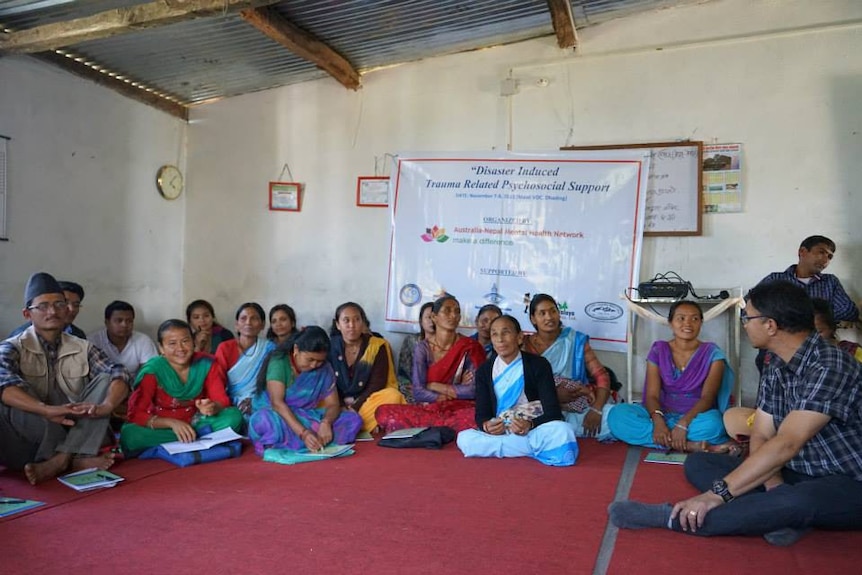 Nepalese people sitting on a mat on the floor in front of a sign about trauma related psychosocial support