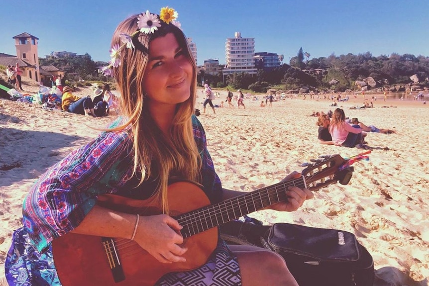 Long-haired woman with daisy chain in her hair plays guitar on a beach