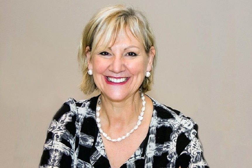 Head and shoulders view of a blonde woman smiling, wearing a black and white top and white necklace.