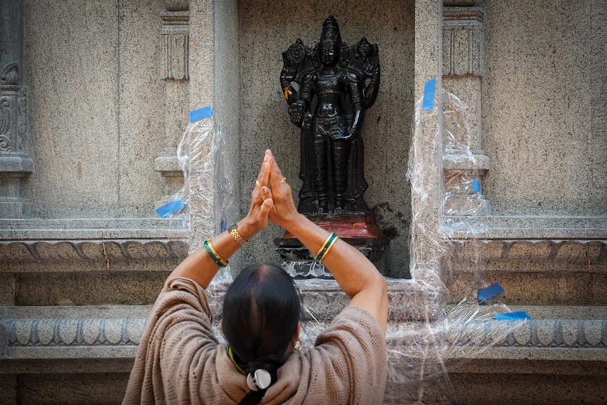 A woman places her palms together over her head while looking at a small Hindu statue