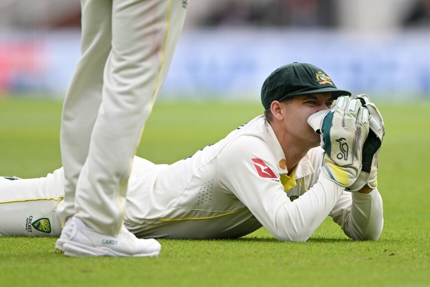 Australia wicketkeeper Alex Carey covers his face as he lies on the ground after dropping a catch during a Test.