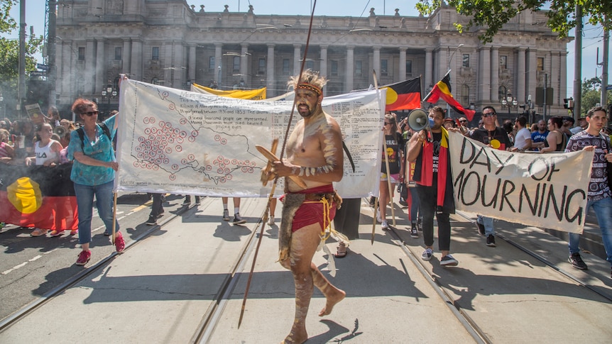 Aboriginal people holding flags and banners march outside Parliament House in Melbourne.
