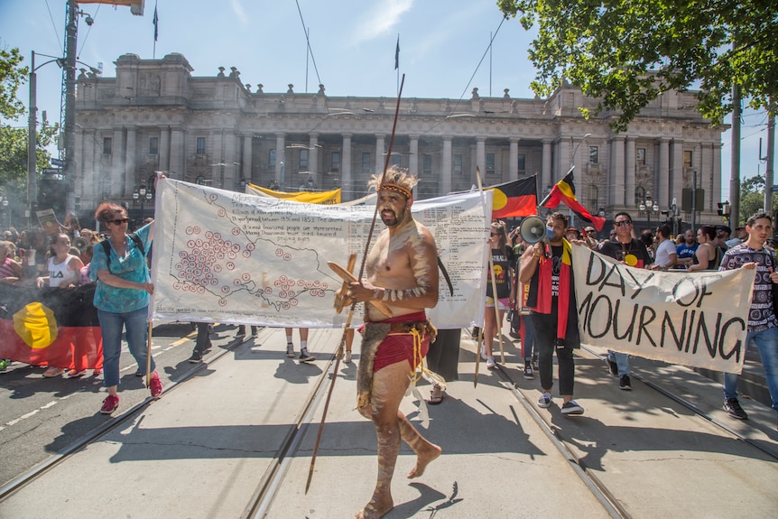 Aboriginal people holding flags and banners march outside Parliament House in Melbourne.