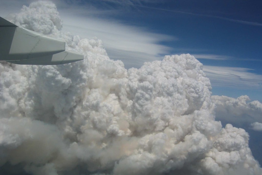 Bushfire smoke billows in the air like clouds. The photo is taken from inside a plane