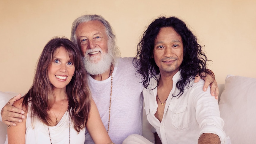 Portrait of middle-aged Caucasian couple with Nepalese man. All are wearing loose light-coloured clothing and have wavy hair.