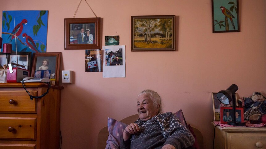 Bev Howlett with pictures on the wall above head at the Wintringham Aged Care Hostel in Williamstown, Victoria.