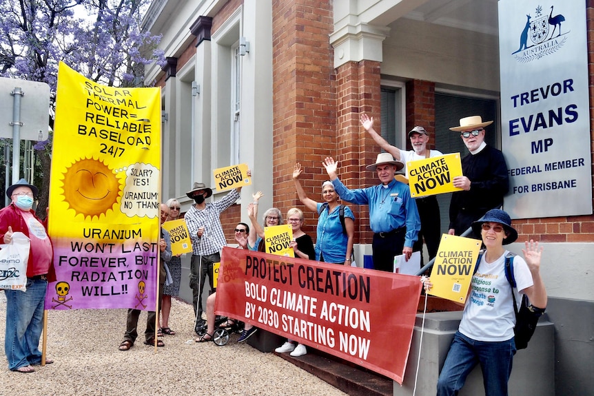 A group of people holding climate change banners demonstrate outside a politician's office