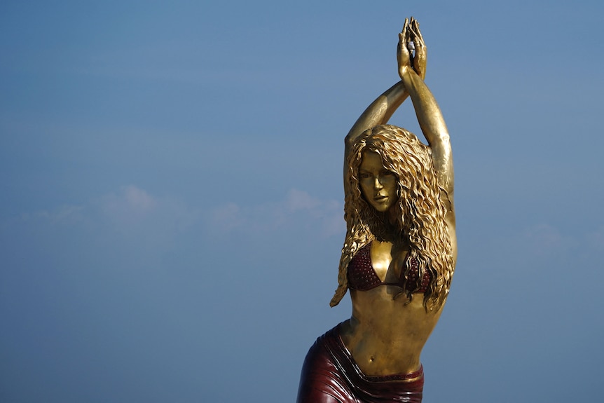 A view of a bronze statue of Shakira. She's in a sarong and bikini top. Her hair is long and she's in the middle of dancing.