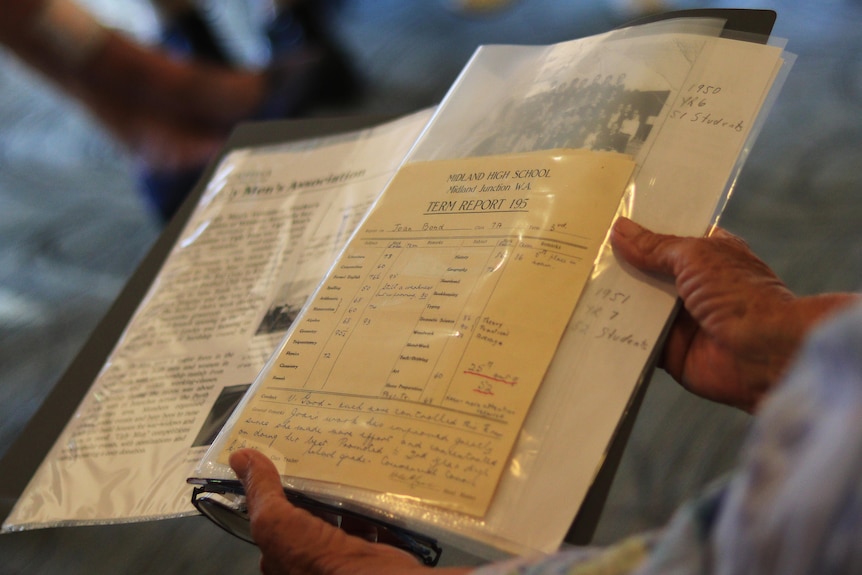 A photo of a folder containing an old, yellowed report card as well as newspaper clippings